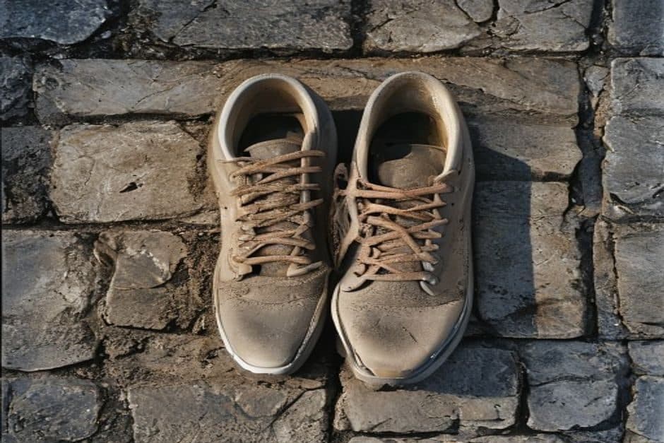 Une paire de chaussures de course usées posée sur une marche en pierre, semelles marquées au talon