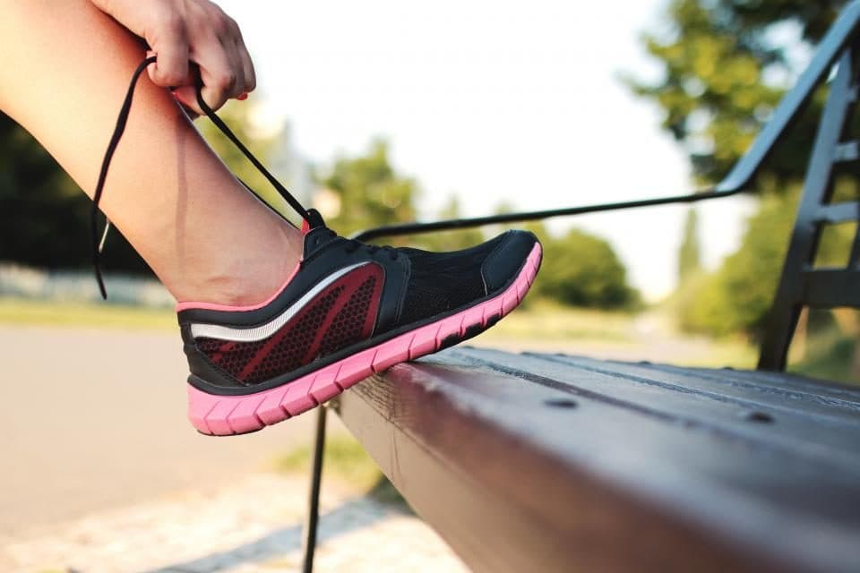 Une main qui lace une chaussure de running posée sur un banc, en gros plan