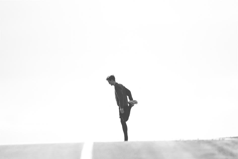 Silhouette d'un coureur en train de s'étirer, en noir et blanc sur un ciel clair